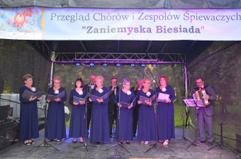 Grupa kobiet w identycznych, ciemnoniebieskich sukienkach na scenie.