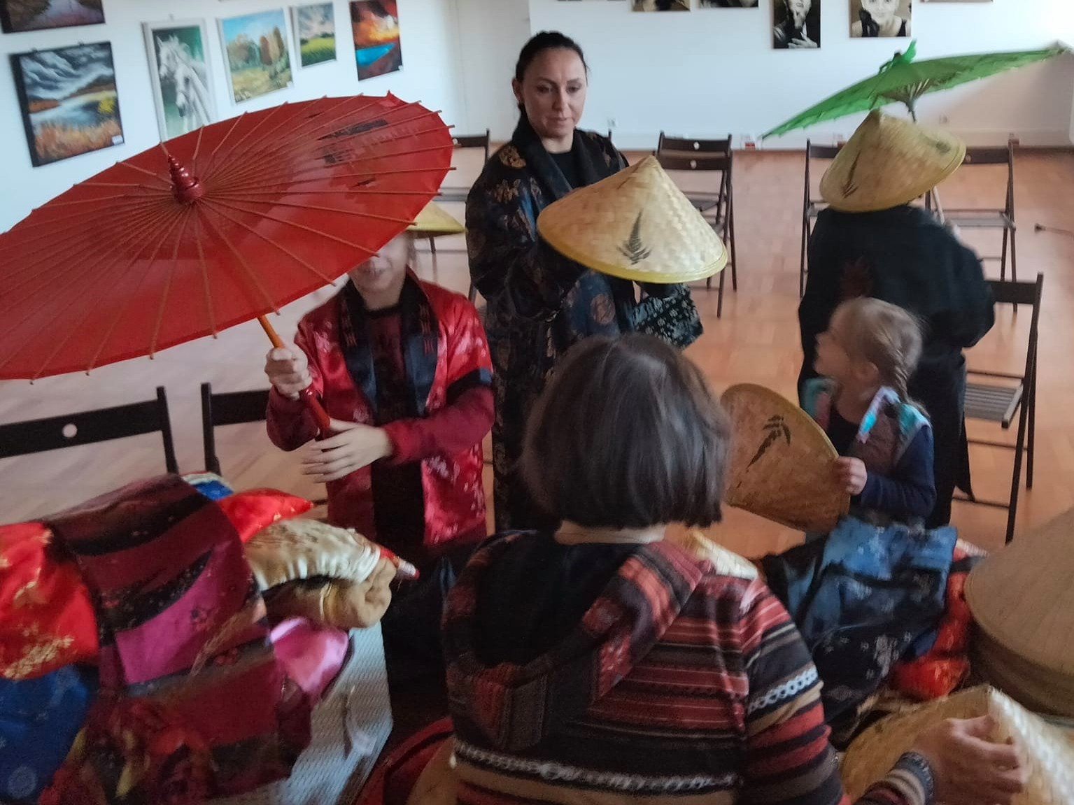 Dzieci podczas warsztatów przybliżających kulturę Chin przymierzają stożkowe kapelusze oraz parasolki