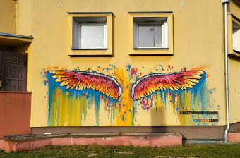 Grafiti przedstawiające tęczowe skrzydła umieszczone na ścianie budynku.