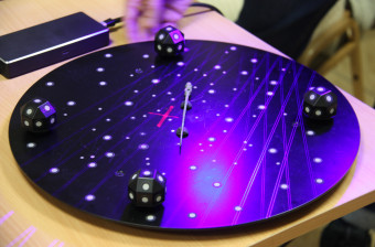 Zabytkowa spinka na środku czarnego koła, oświetlana z różnych stron niebieskim i fioletowym światłem