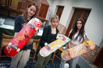 Trzy dziewczyny trzymają ręcznie malowane deski skateboard w jaskrawych barwach